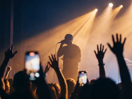 A singer in silhouette under warm stage lights, the crowd’s hands raised